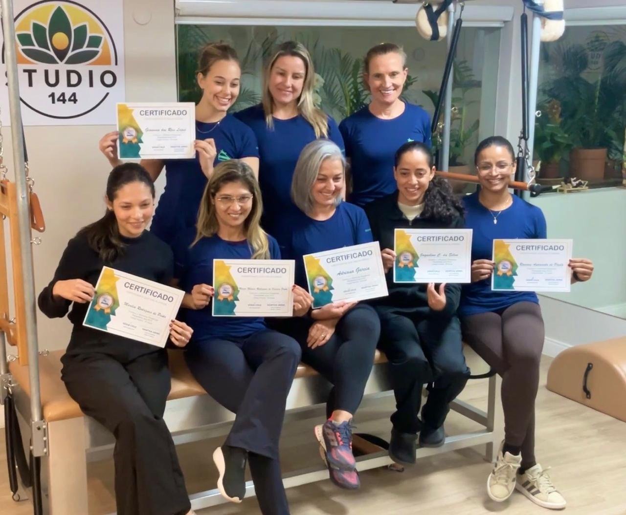 Participantes do workshop de fevereiro de 2024 sorrindo e segurando seus certificados, sentados em um aparelho de Pilates.
